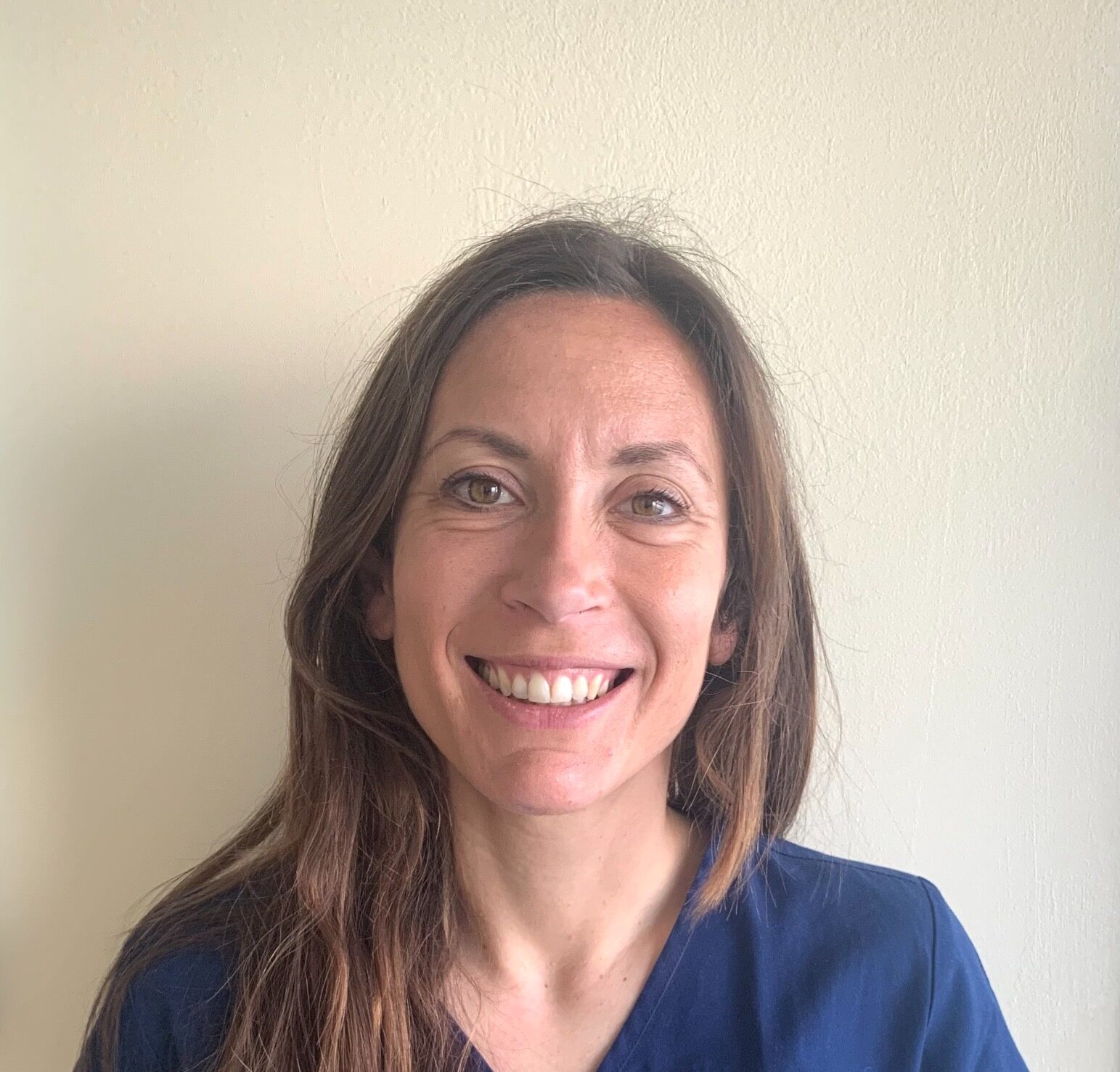 Eleonora Gili tecnico veterinario e front office manager dell'Ospedale Veterinario Ardenza, una donna dai lunghi capelli castani, che indossa un top blu navy, sorride alla telecamera mentre si trova di fronte a un semplice muro chiaro.